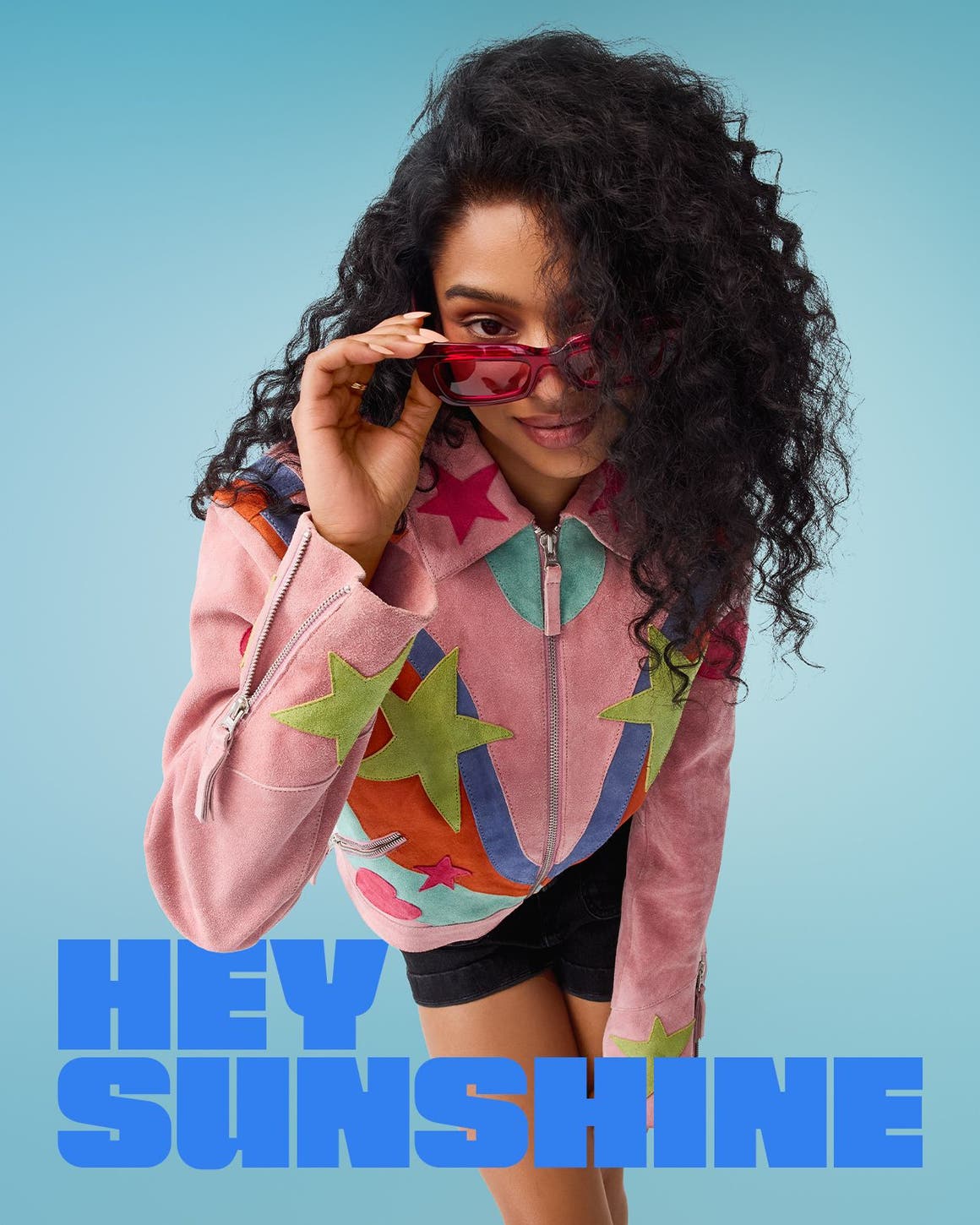 A woman wearing red sunglasses, a colorful jacket and black shorts.