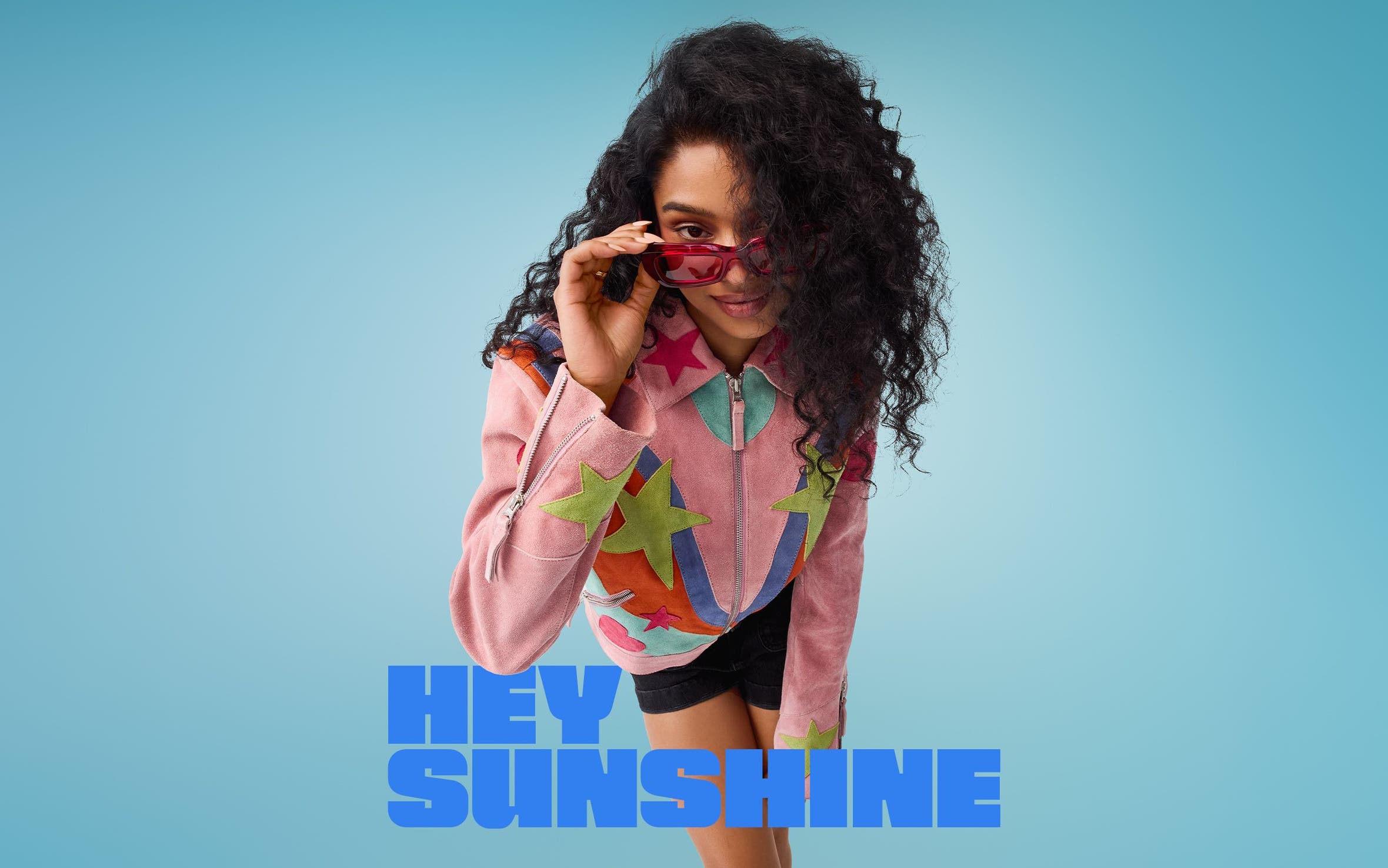 A woman wearing red sunglasses, a colorful jacket and black shorts.