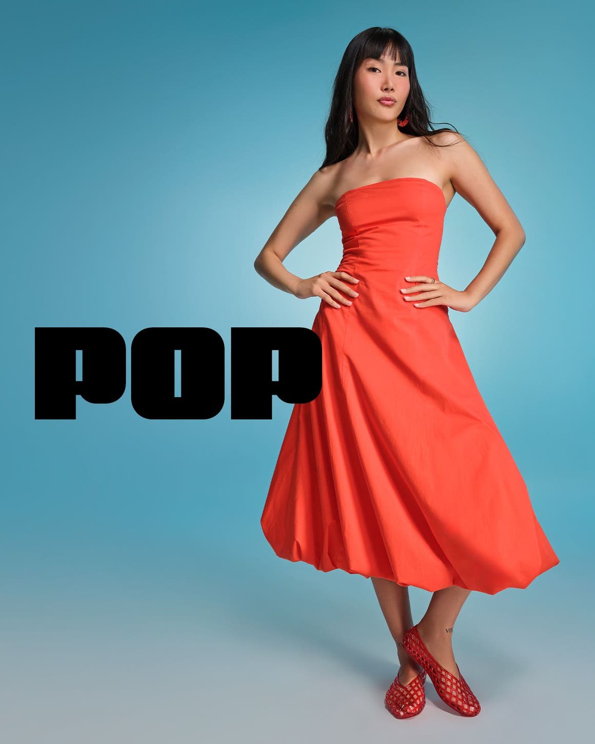 A woman wearing a strapless orange midi dress with red jelly slip-ons.