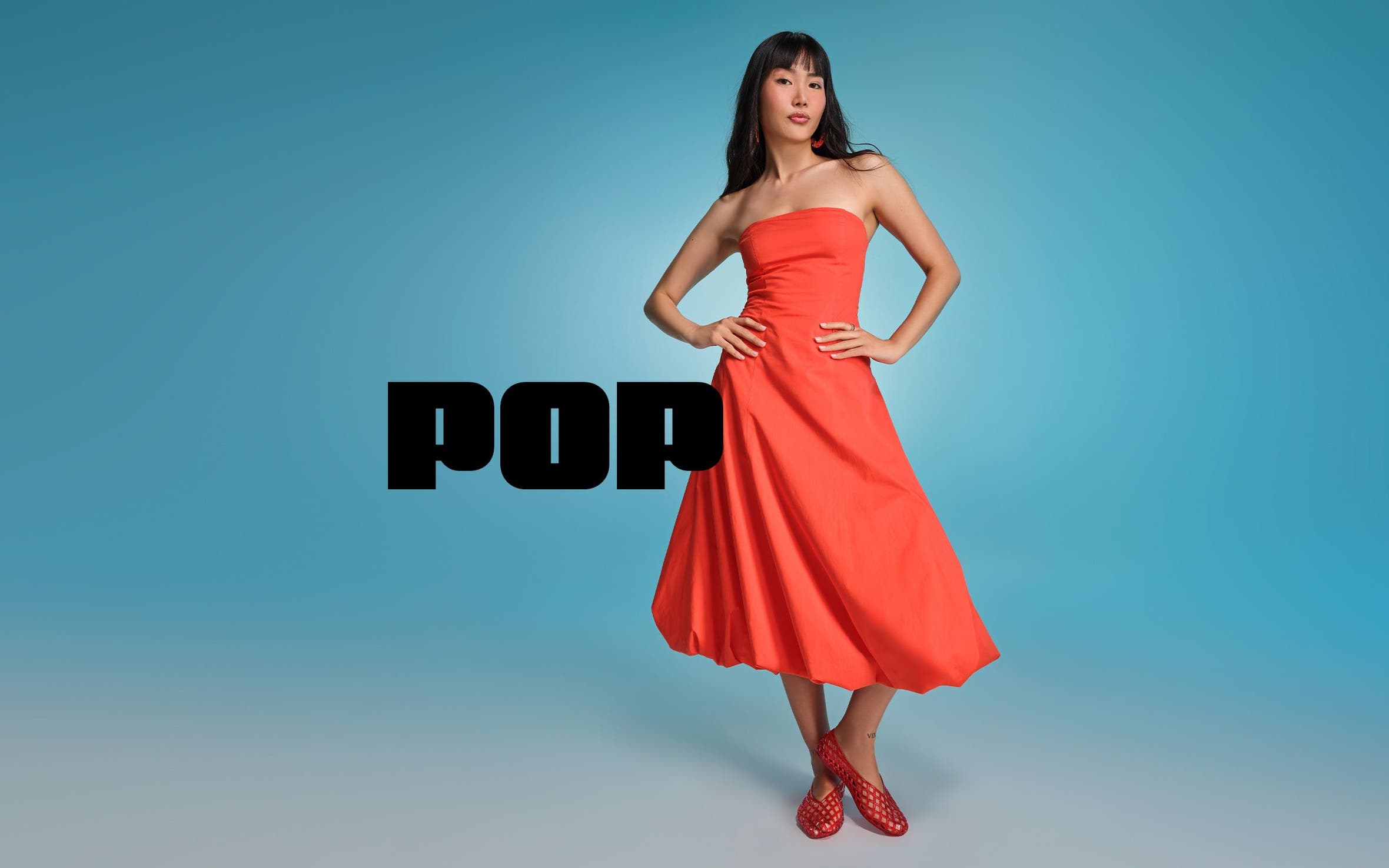 A woman wearing a strapless orange midi dress with red jelly slip-ons.
