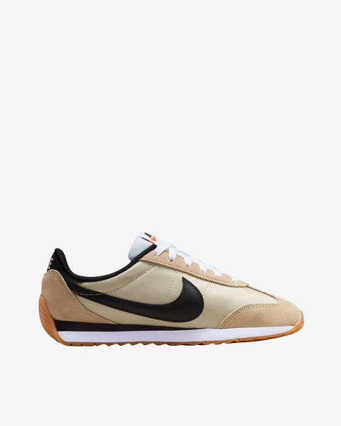 A Nike Cortez sneaker in tan/khaki with black swoosh and gum sole.