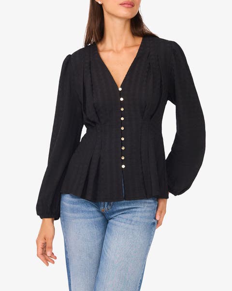 Woman wearing a black long-sleeve blouse with a V-neck, and a fitted waist with a slight peplum flare.