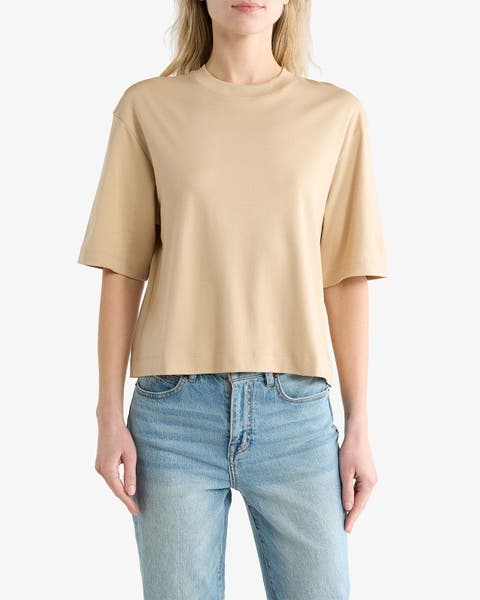 Woman wearing a beige crew‑neck T-shirt with a boxy, slightly cropped fit and elbow-length sleeves, paired with light-wash jeans.