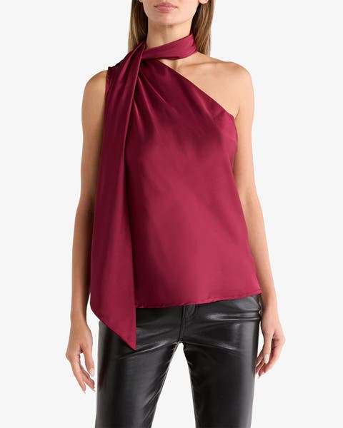 Woman wearing a burgundy satin one‑shoulder top with an asymmetric halter neckline and long draped neck tie, styled with black leather pants.