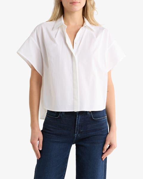 Woman wearing a white short-sleeve button-up shirt with a boxy, slightly cropped fit, paired with dark-wash jeans.