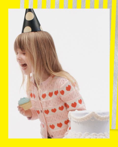 A girl wearing a cardigan and party hat with a cupcake.