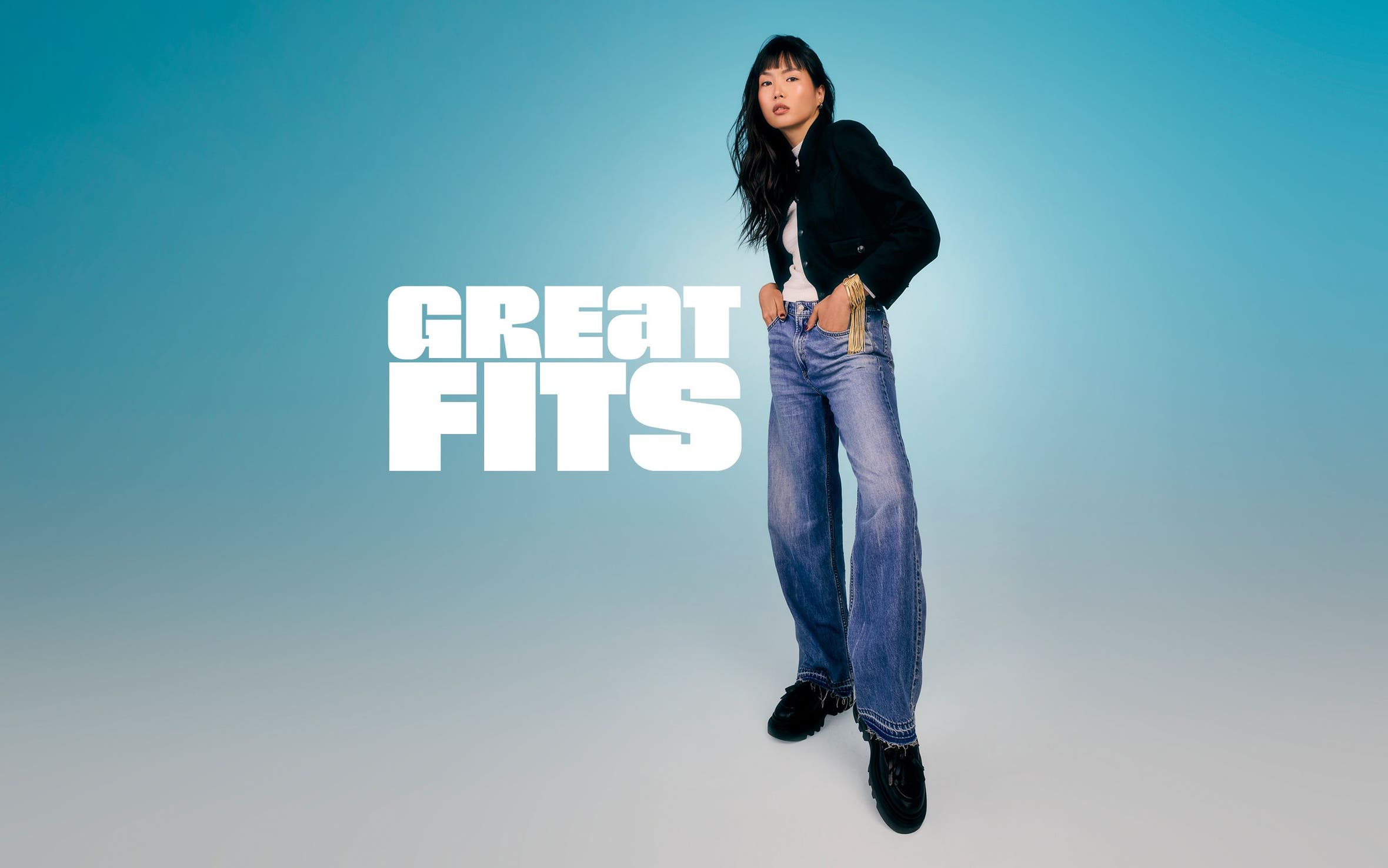 A woman wearing wide-leg light wash jeans and a black cropped jacket.