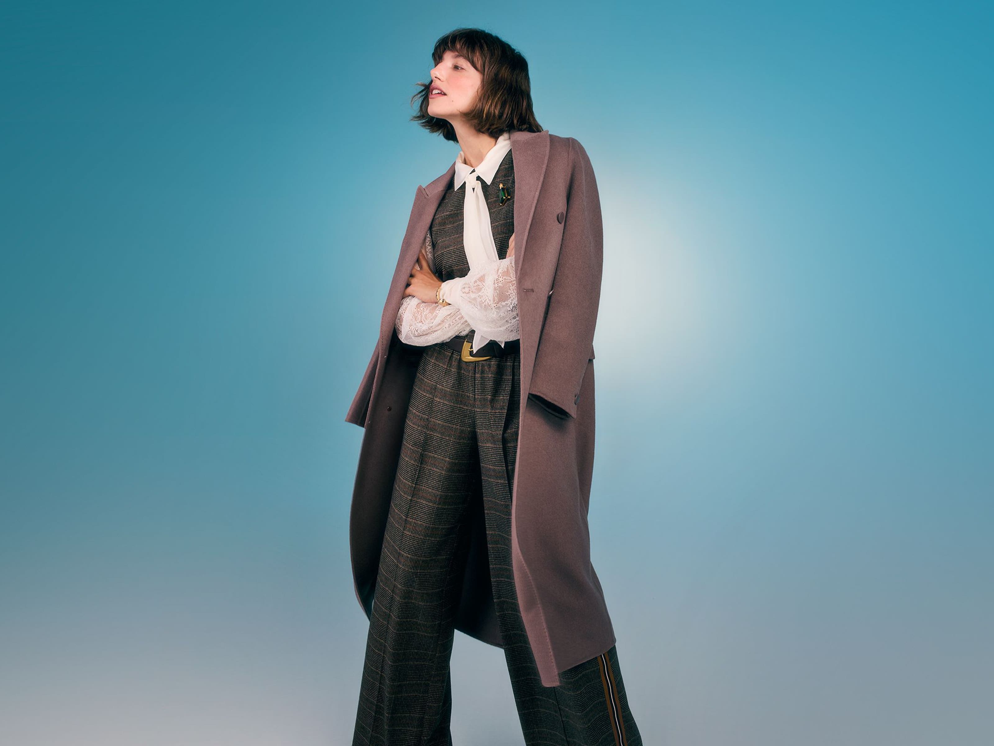 A woman wearing a suit vest with matching pants, a white shirt and overcoat.