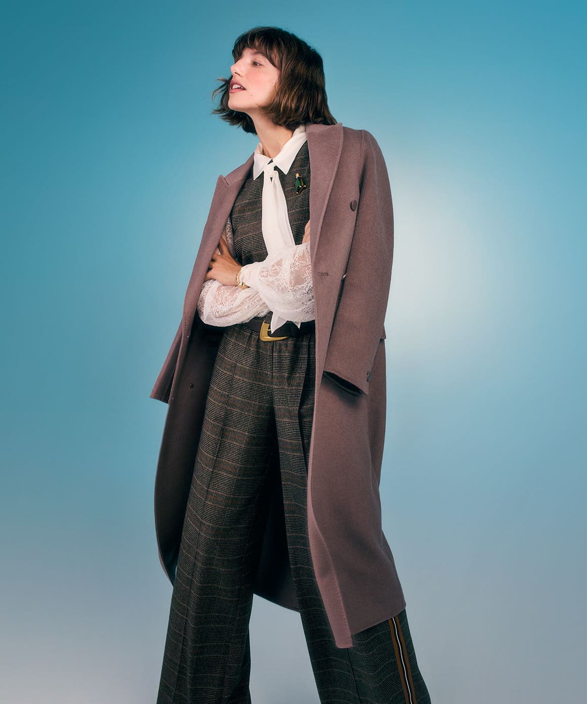 A woman wearing a suit vest with matching pants, a white shirt and overcoat.