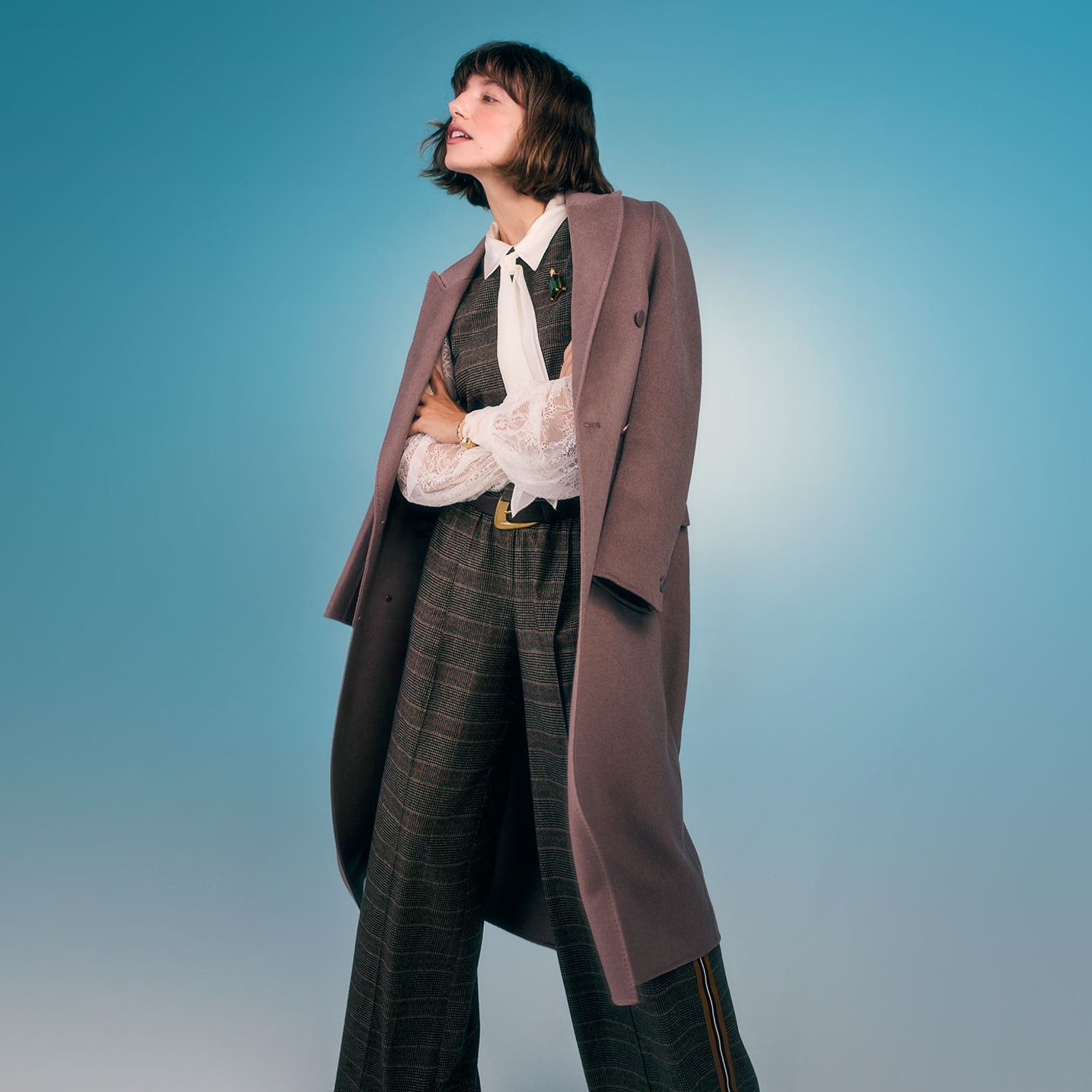A woman wearing a suit vest with matching pants, a white shirt and overcoat.