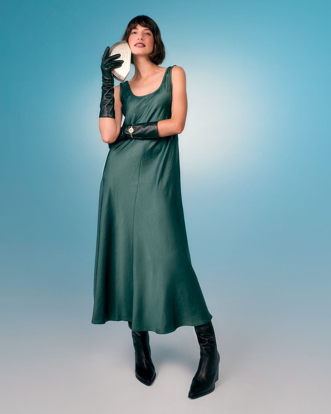 A woman wearing a silky green dress with black boots.