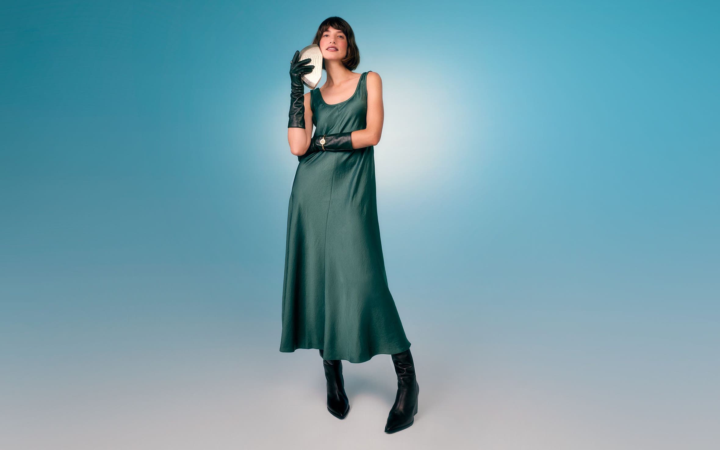 A woman wearing a silky green dress with black boots.