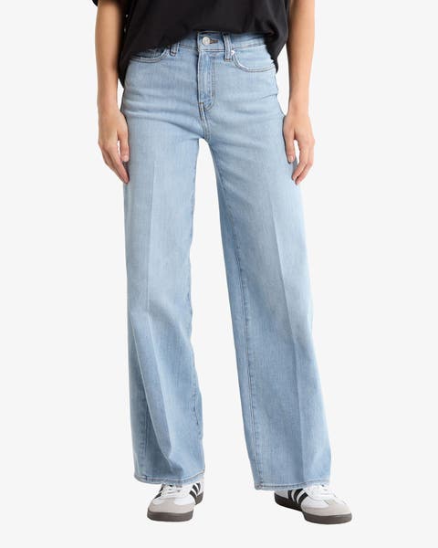 A woman wearing wide-leg jeans and sneakers.