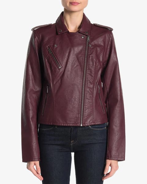 Woman wearing a burgundy faux‑leather moto jacket with an asymmetrical front zipper.