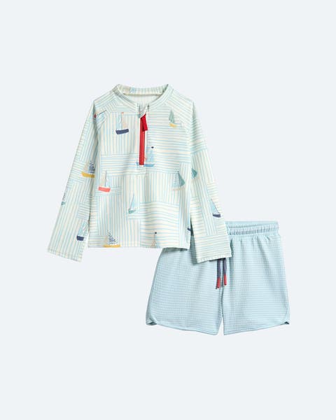 A sailboat-printed rash guard and light blue swim trunks.