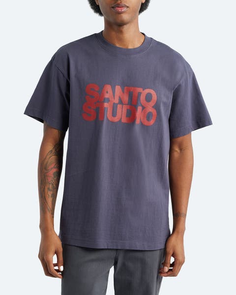 A man wearing a logo T-shirt from Santo Studio.