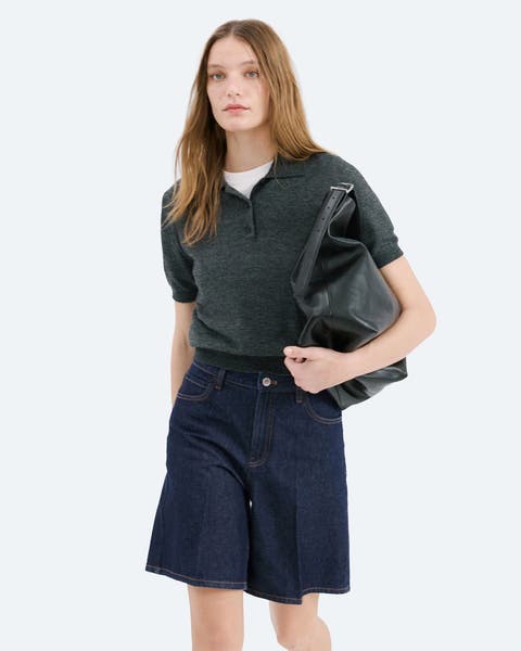 A woman wearing a short sleeve polo and denim shorts.