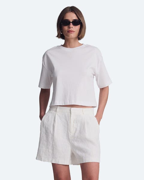 A woman wearing white linen shorts and a white tshirt.