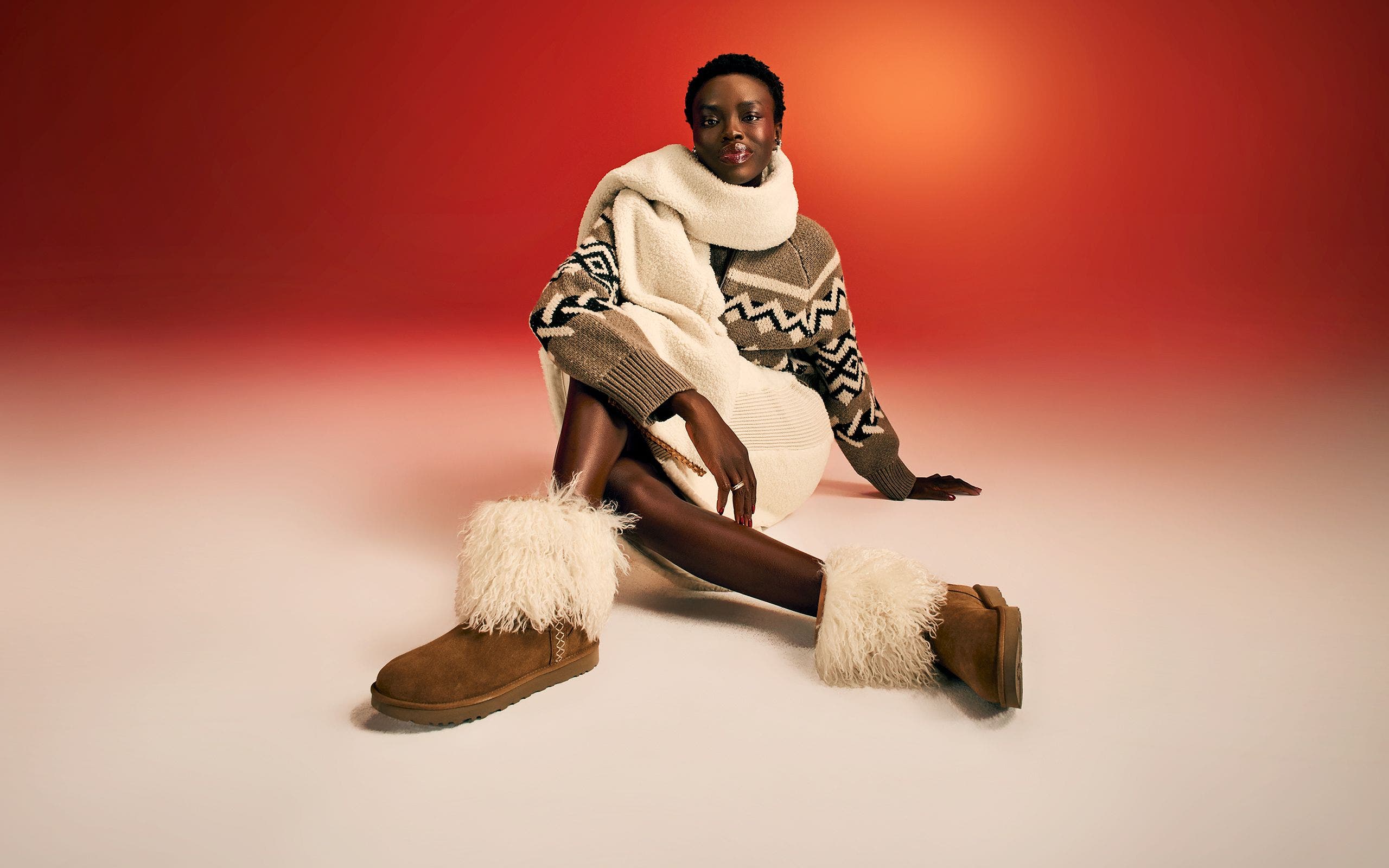 A woman wearing a sweater, a scarf and a pair of UGG boots. 