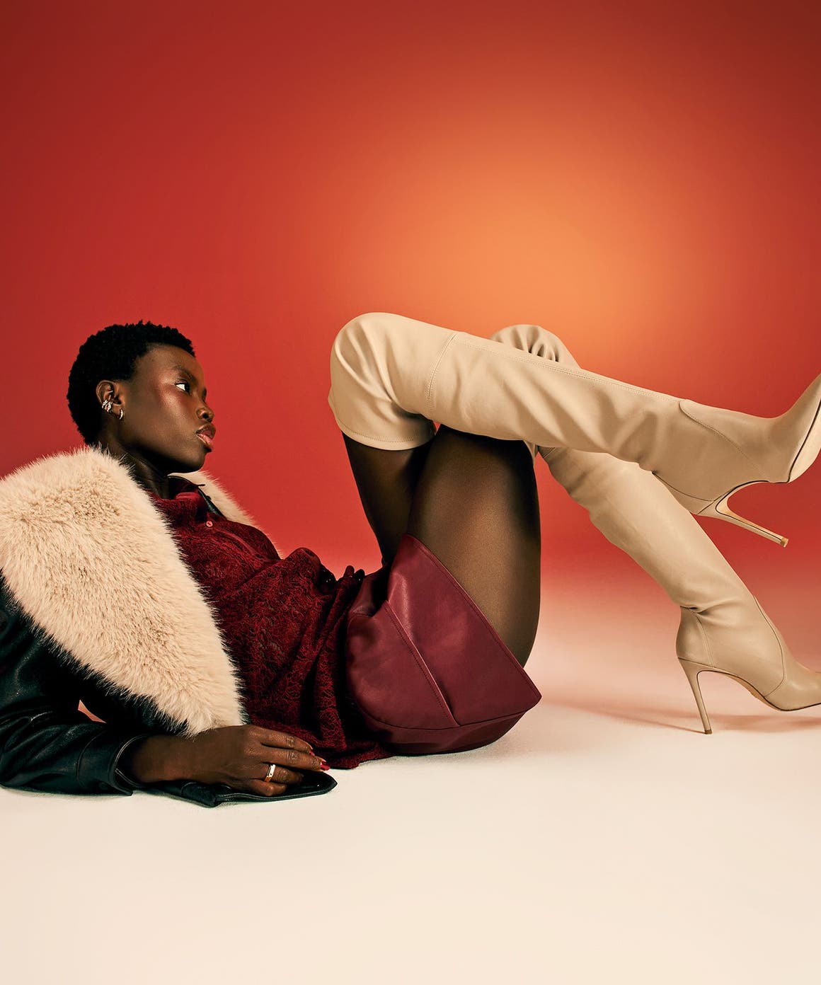 A woman wearing thigh-high boots, a burgundy skirt and a black jacket with a faux-fur collar. 