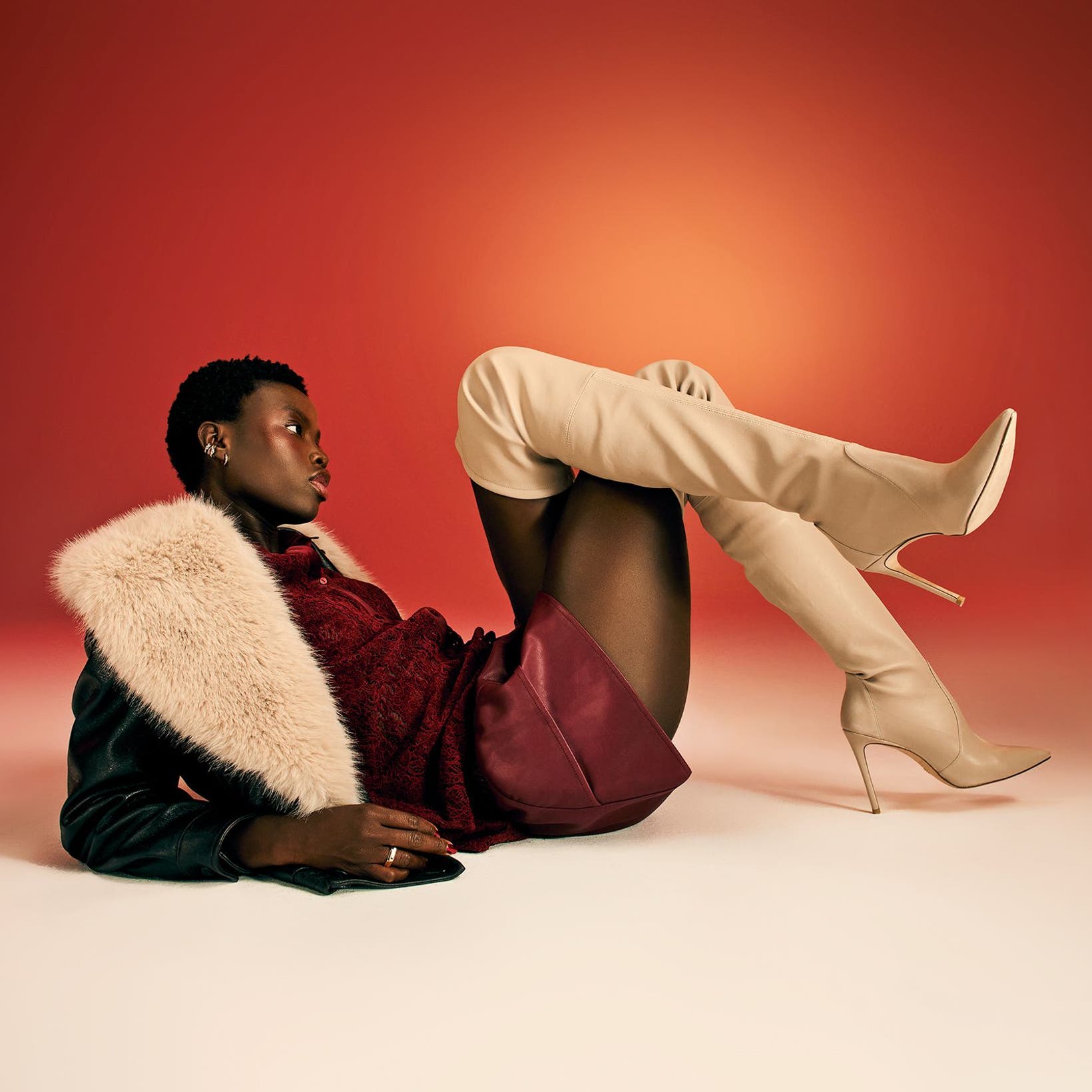 A woman wearing thigh-high boots, a burgundy skirt and a black jacket with a faux-fur collar. 