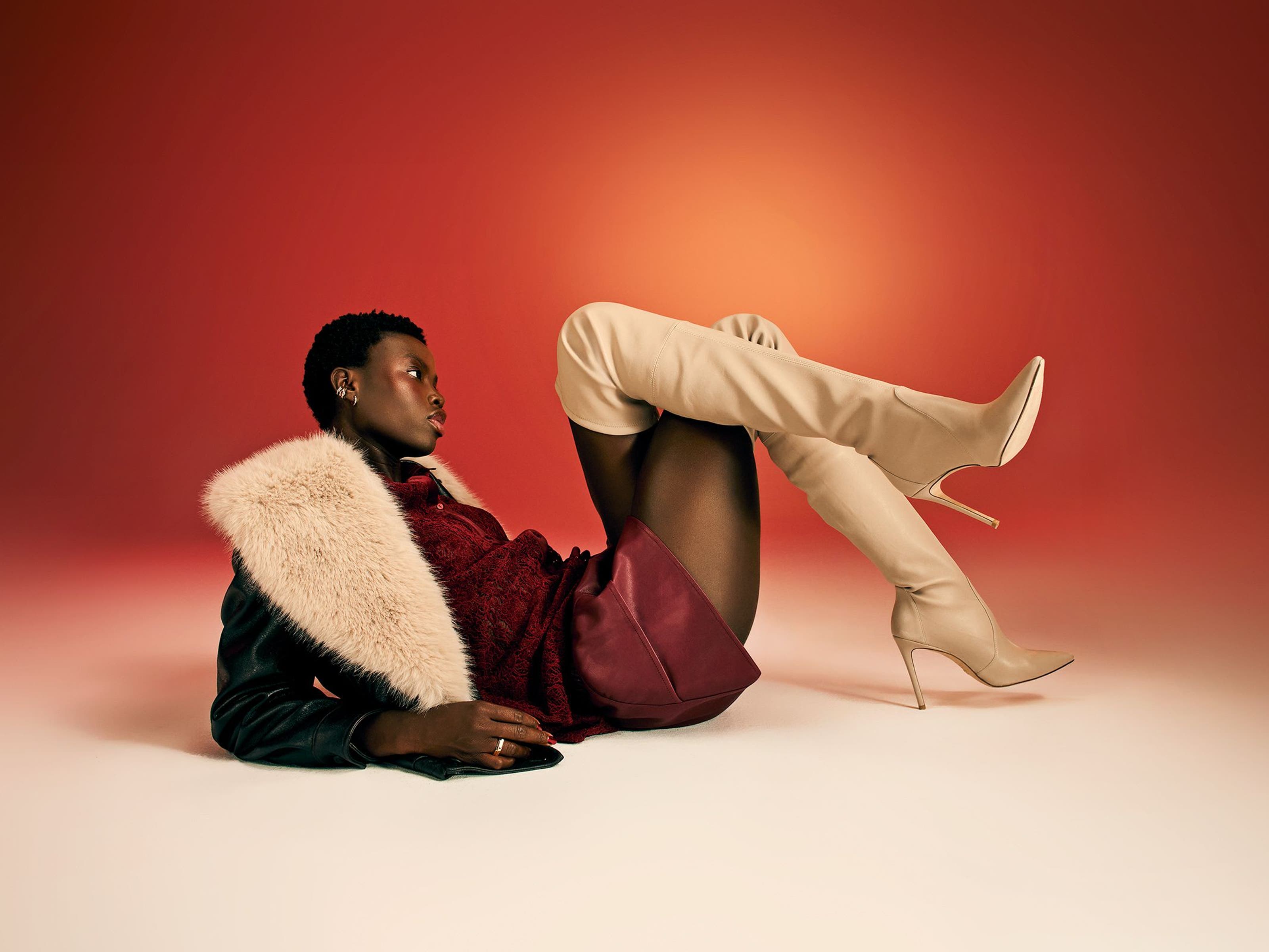 A woman wearing thigh-high boots, a burgundy skirt and a black jacket with a faux-fur collar. 