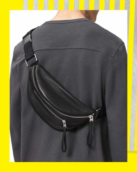 Model wearing black leather sling bag with silver zipper hardware across back.