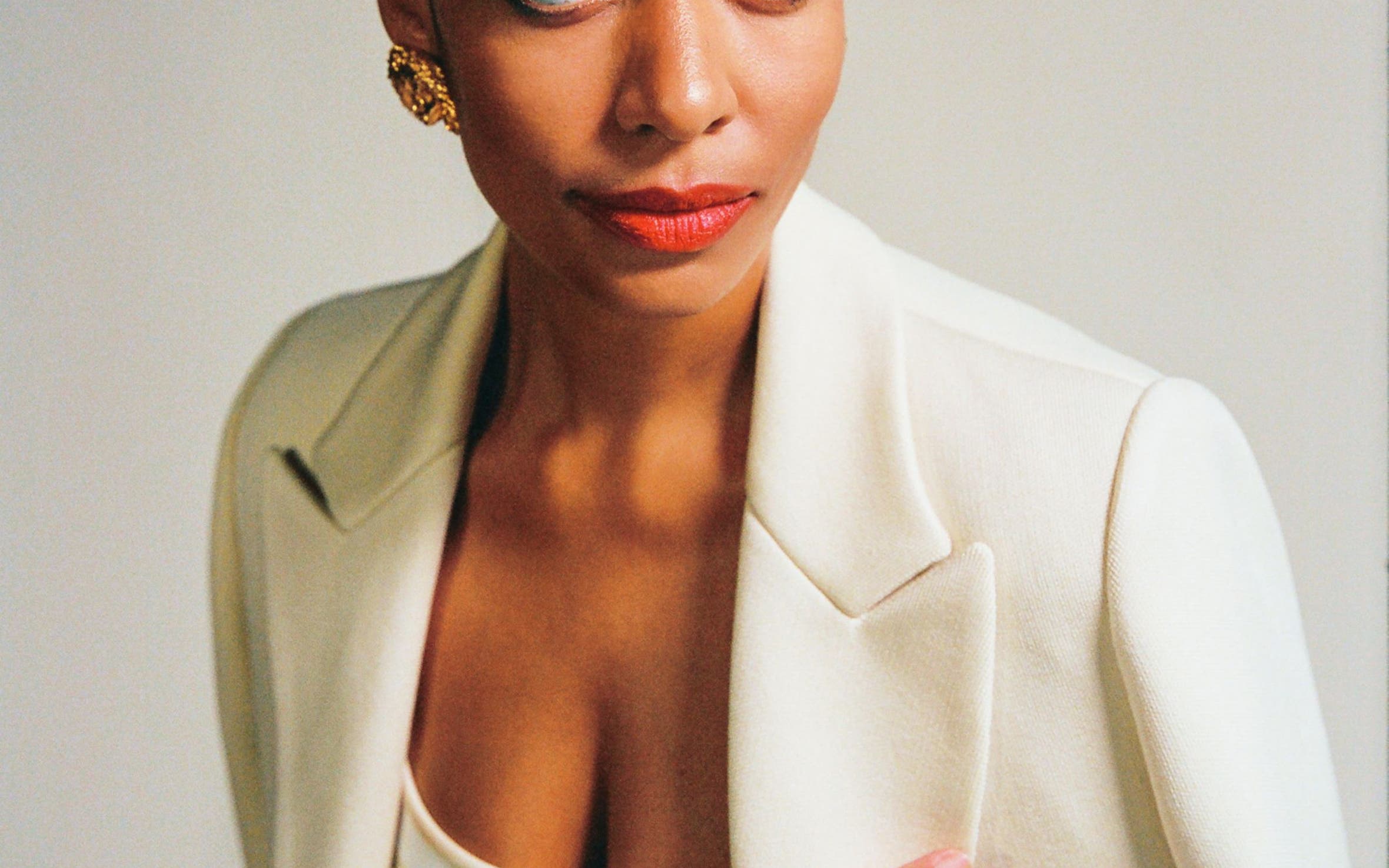 A woman in a white blazer and gold jewelry.