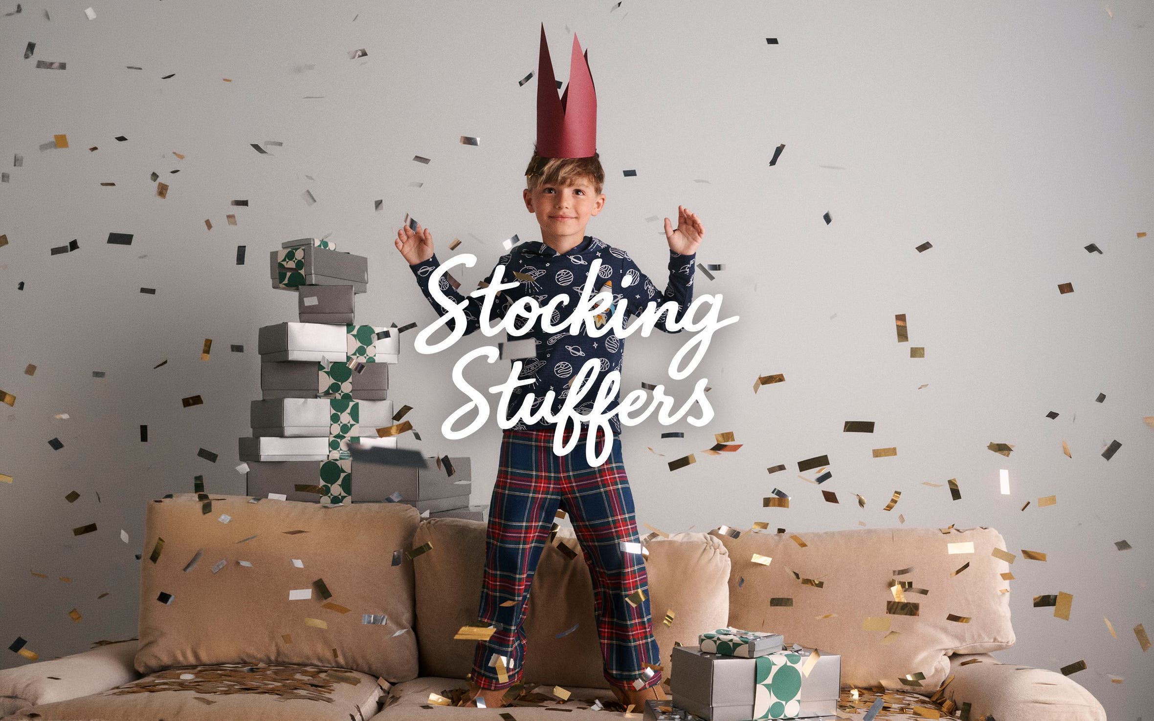 Stocking stuffers. A boy surrounded by confetti and a stack of gifts.