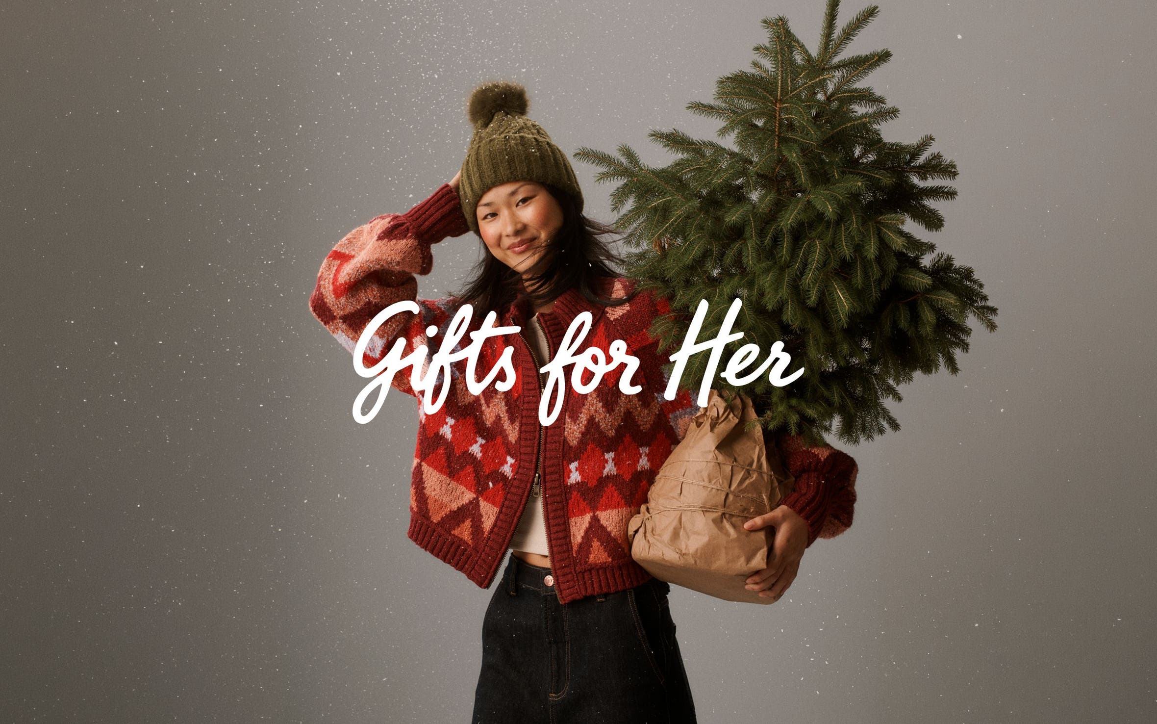 Gifts for her. A woman in winter outerwear holding a small tree.