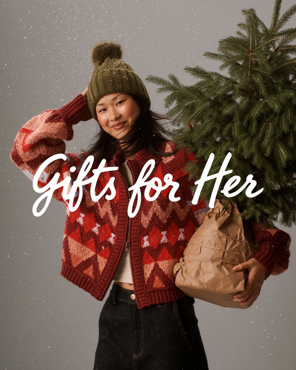 Gifts for her. A woman in winter outerwear holding a small tree.