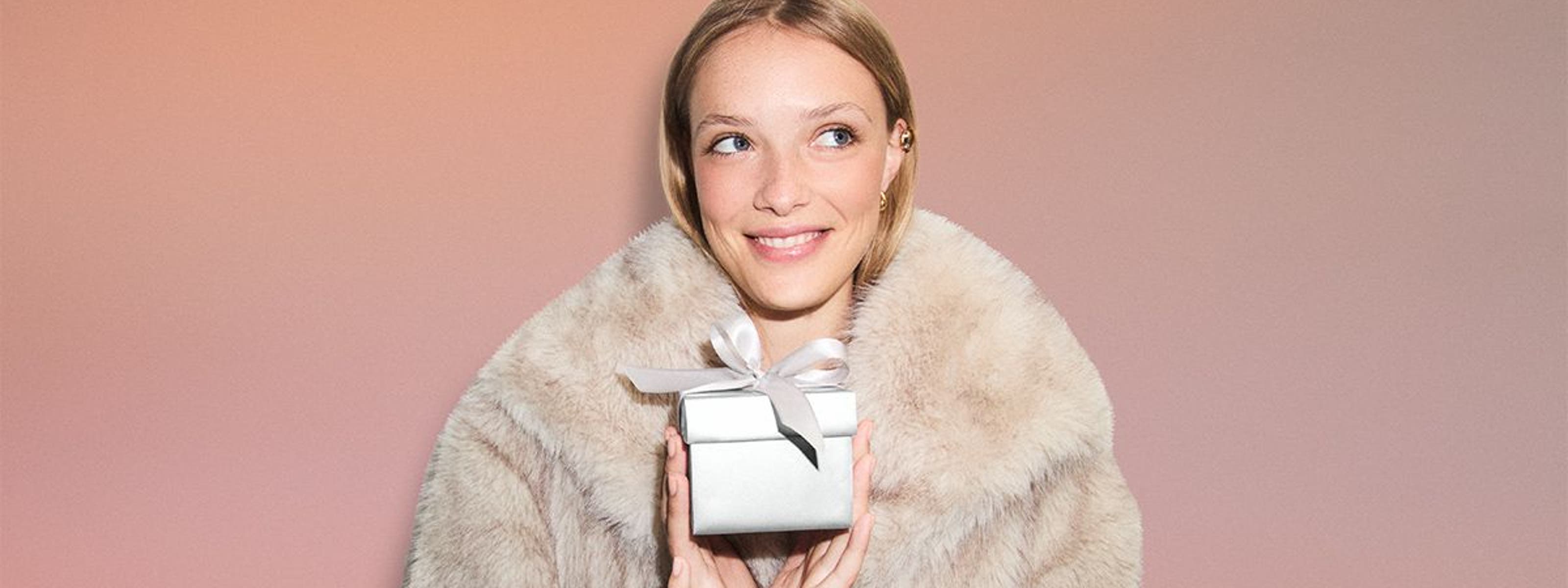 Woman in a faux-fur jacket holding a silver Nordstrom gift box.