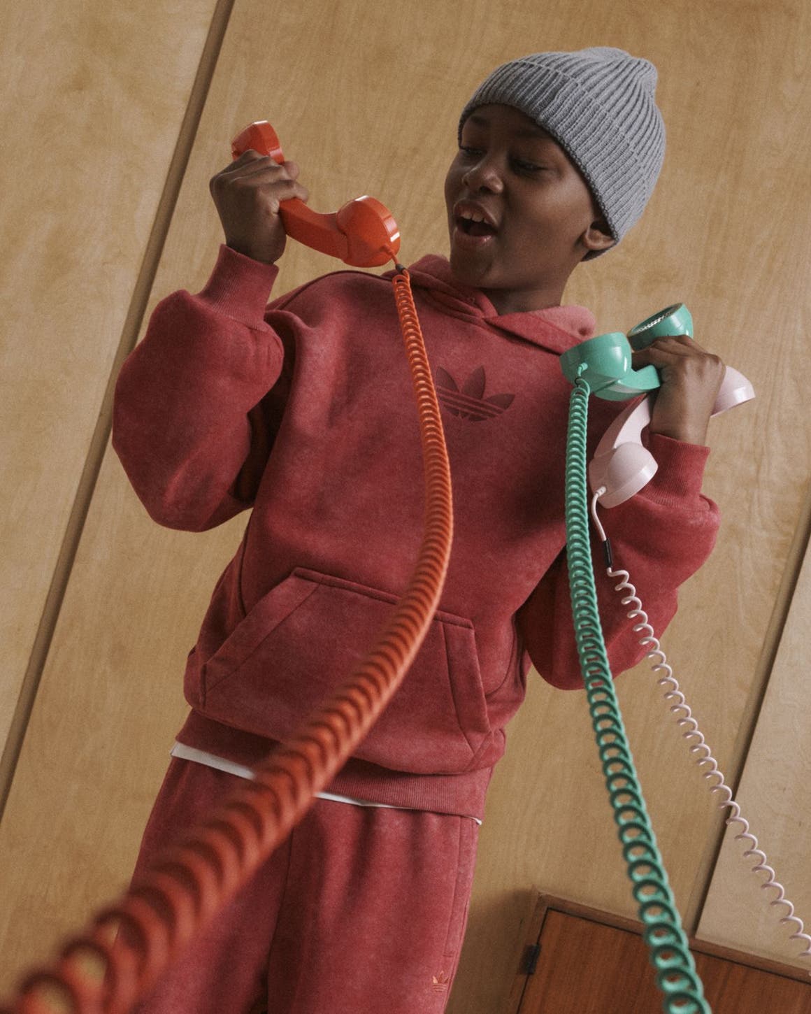 A boy in a sweatsuit holding corded telephones.