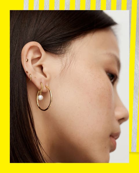 Close-up profile of model wearing stacked gold earrings including a large hoop with pearl drop.