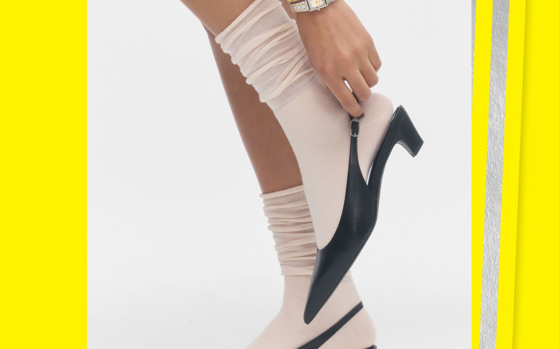 A woman in white socks putting on black kitten-heeled mules.