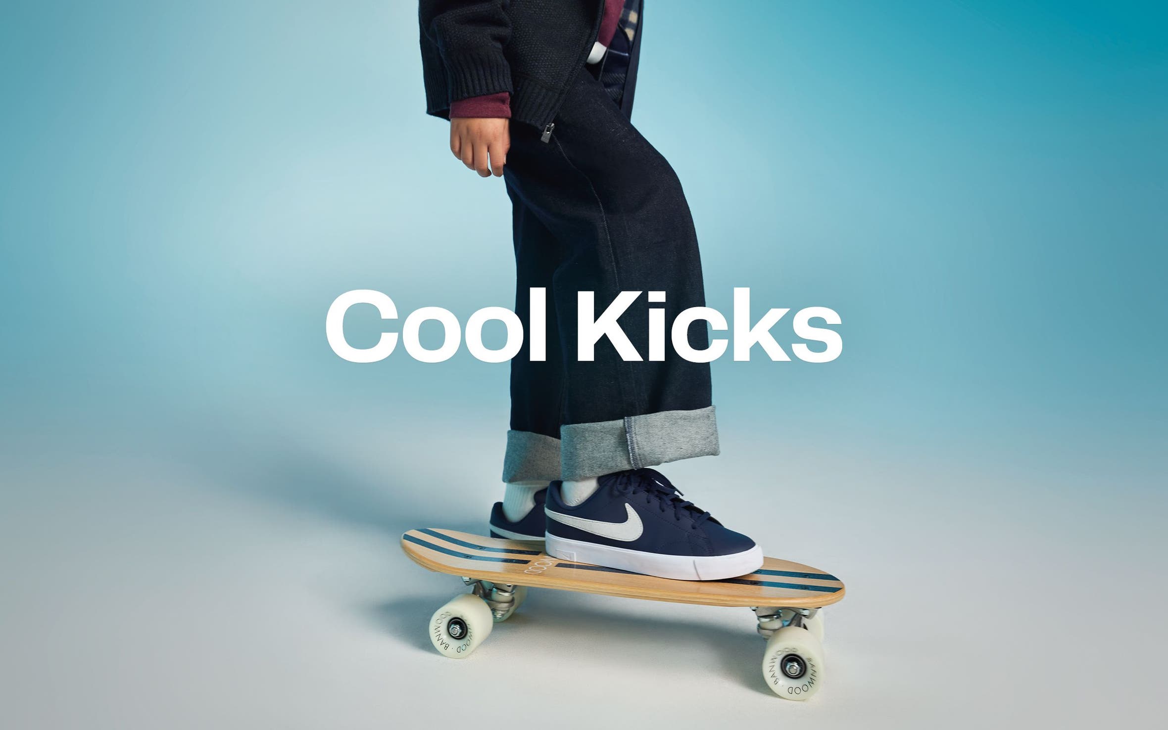 Cool kicks. A kid wearing Nike sneakers stands on a skateboard.  