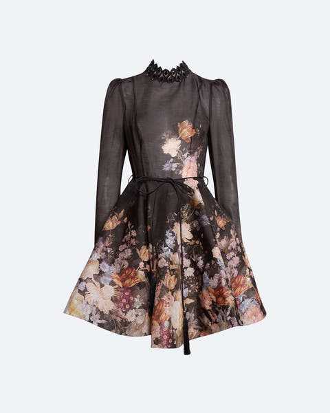Long-sleeve fit-and-flare mini dress with a sheer black high neckline and sleeves, a fitted bodice, and a full pleated skirt in a dark floral print with muted orange, blue, and cream tones, cinched with a thin waist tie.