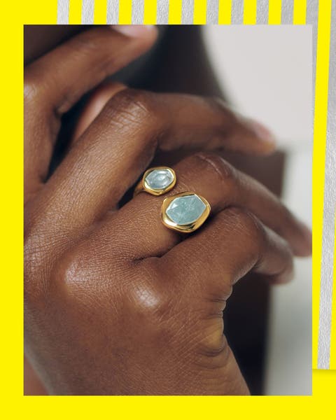 Close-up of model’s hands wearing double-stone gold ring with pale blue gemstones.