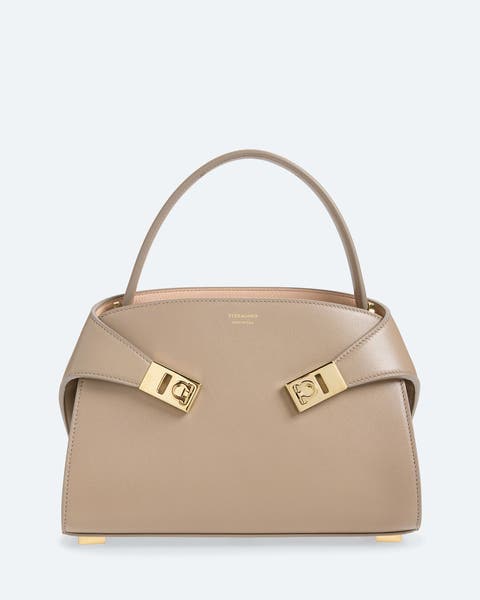 Taupe leather handbag with a structured silhouette, top handle, and gold-tone hardware buckle details on the front