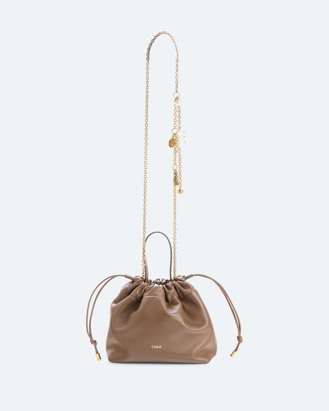Taupe leather bucket bag with a drawstring closure, gold-tone chain and leather strap, and tassel charm details