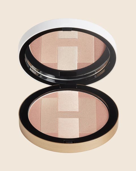 A round gold-rimmed compact in peach and champagne, shown open with its mirrored lid.