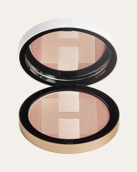 A round gold-rimmed compact in peach and champagne, shown open with its mirrored lid.