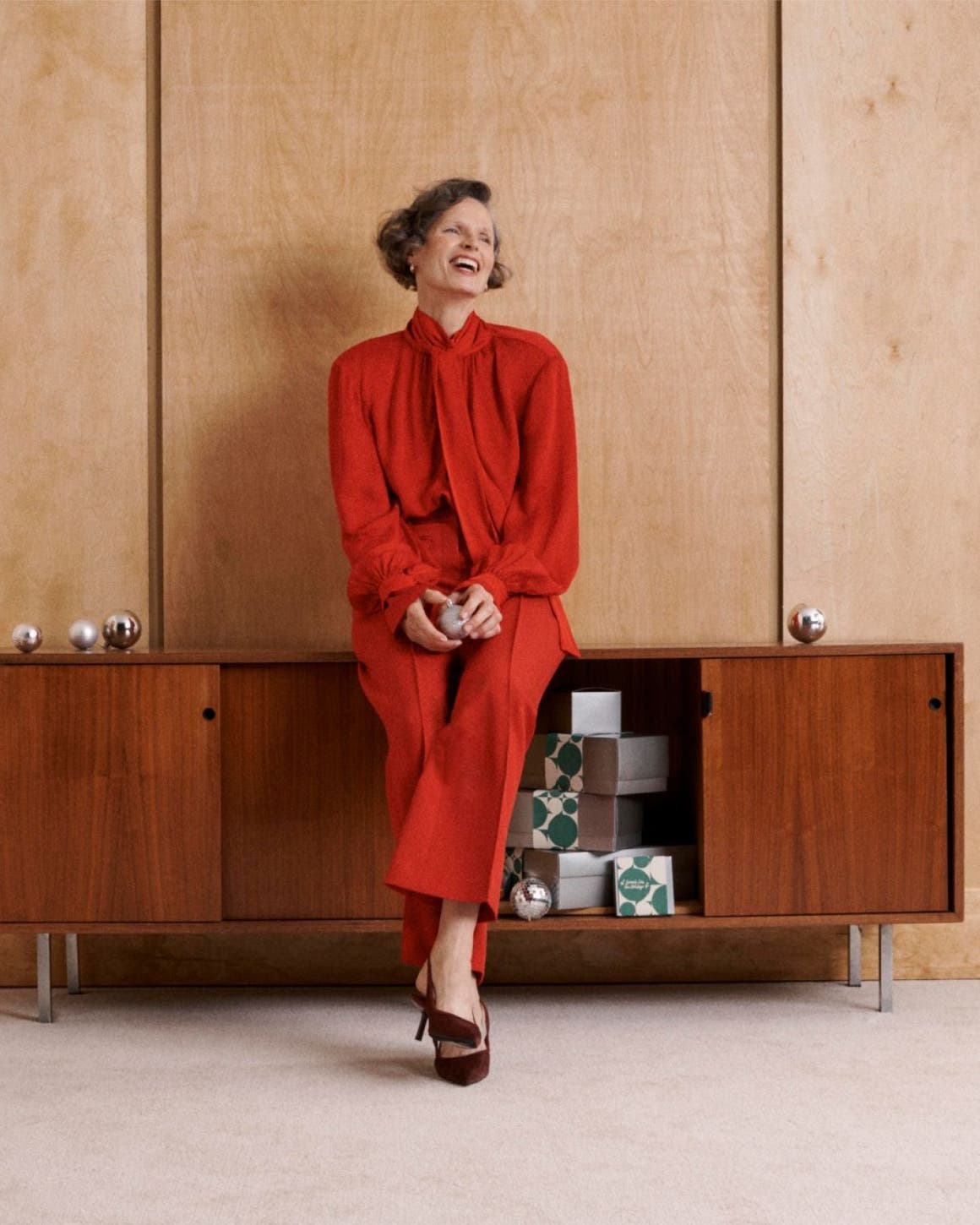A woman leaning against a credenza. 