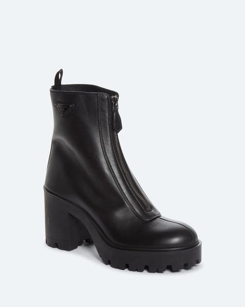 Black leather combat-style boot with a front zip closure, triangular logo detail, and a chunky lugged sole with block heel.