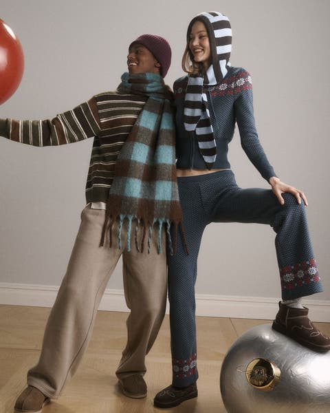 A man and woman wearing scarves, sweaters, pants and slippers.