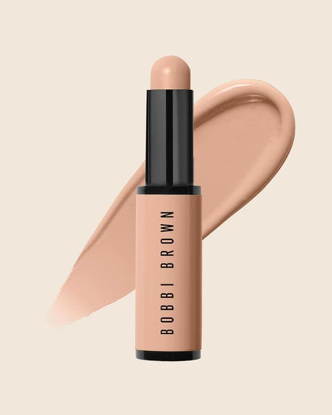 A Bobbi Brown concealer stick in a peach tube with a black cap and a matching swatch.