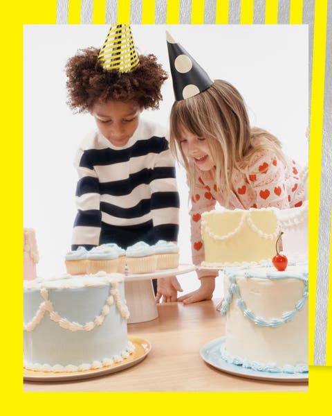 A boy and girl in party hats looking at birthday cakes.