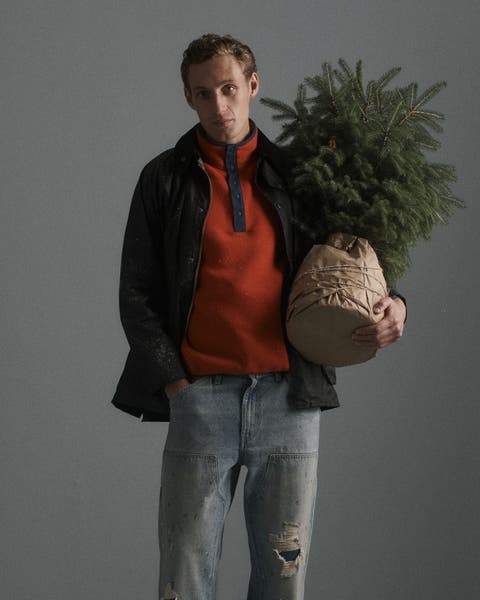 A man wearing a sweater, jacket and jeans holding a tree.