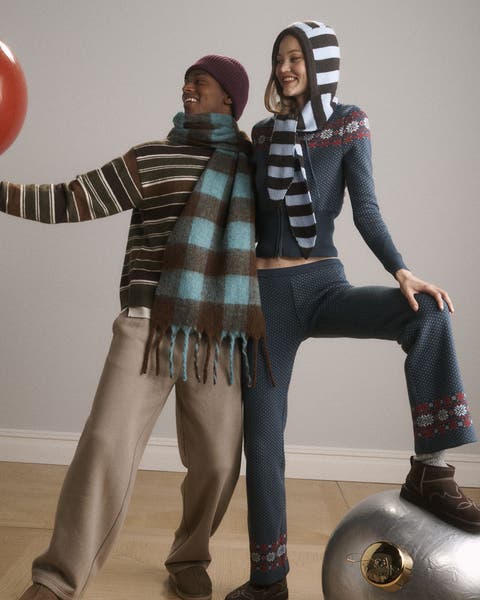 A man and woman wearing scarves, sweaters, pants and slippers.