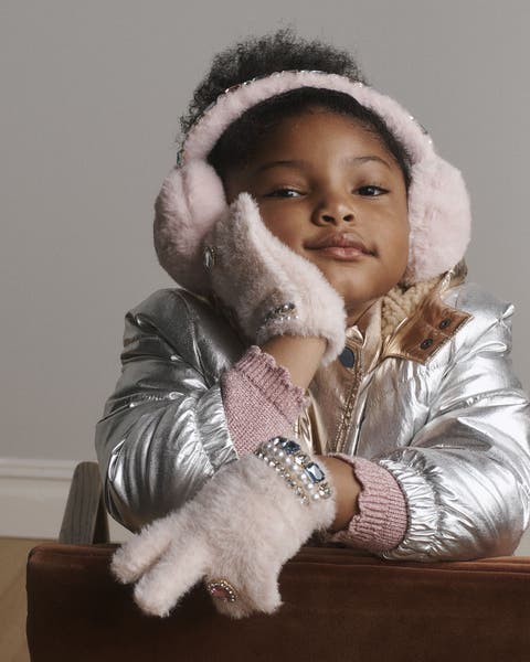 A girl wearing earmuffs, gloves and a silver jacket.